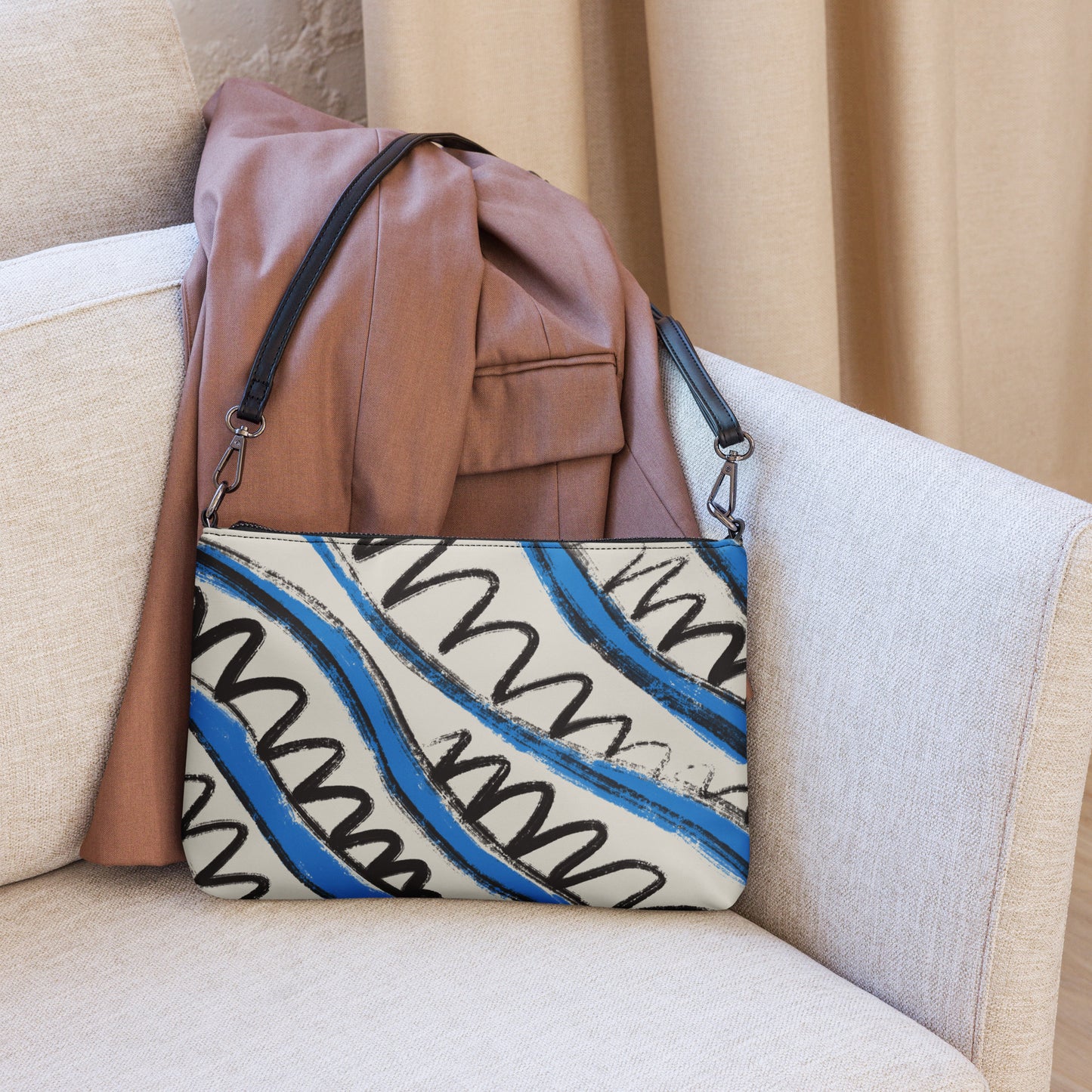Panther & Palm crossbody bag in graphic tropical print resting on a neutral sofa beside a brown blazer.