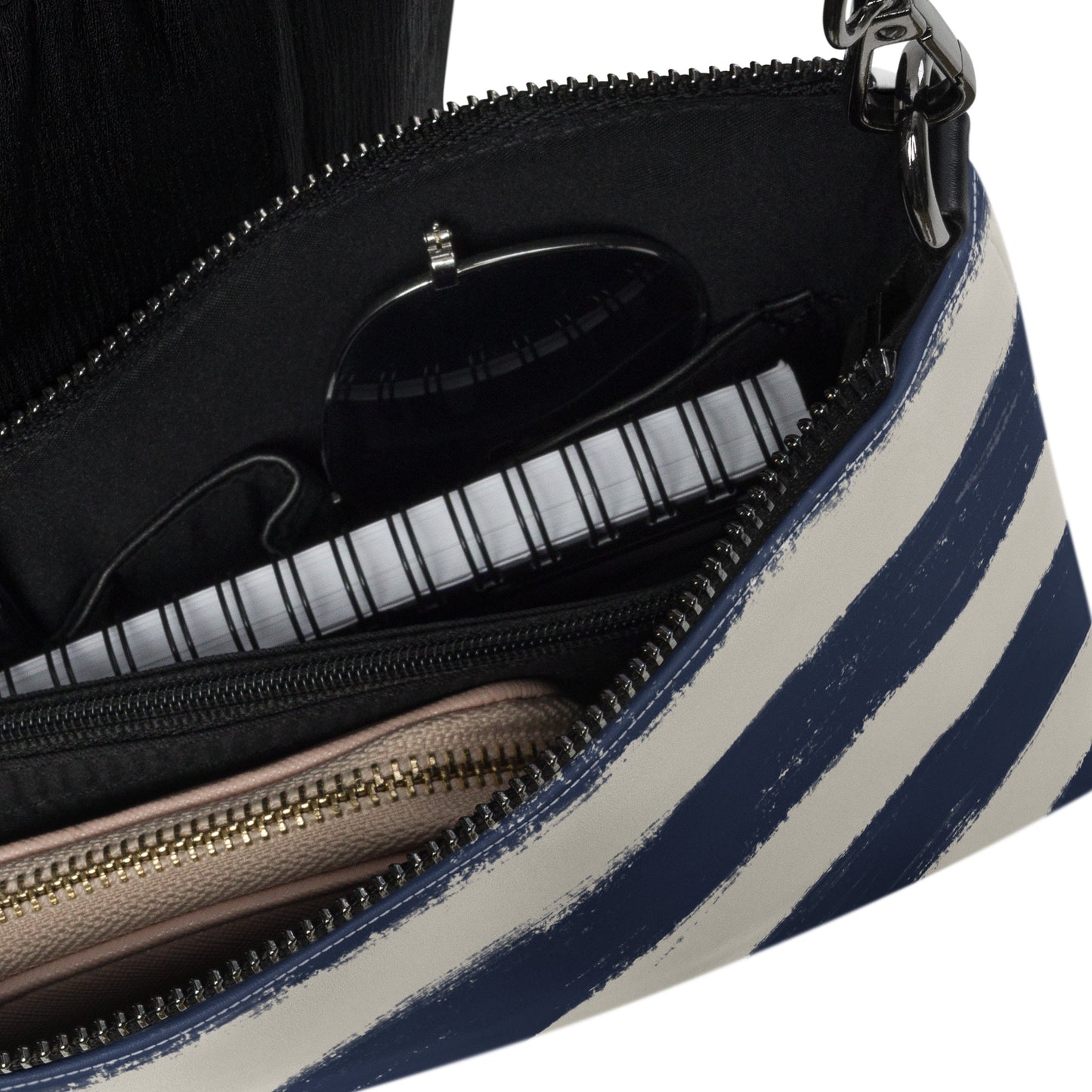 Interior of crossbody bag showing zippered compartments with sunglasses, wallet, and notebook inside