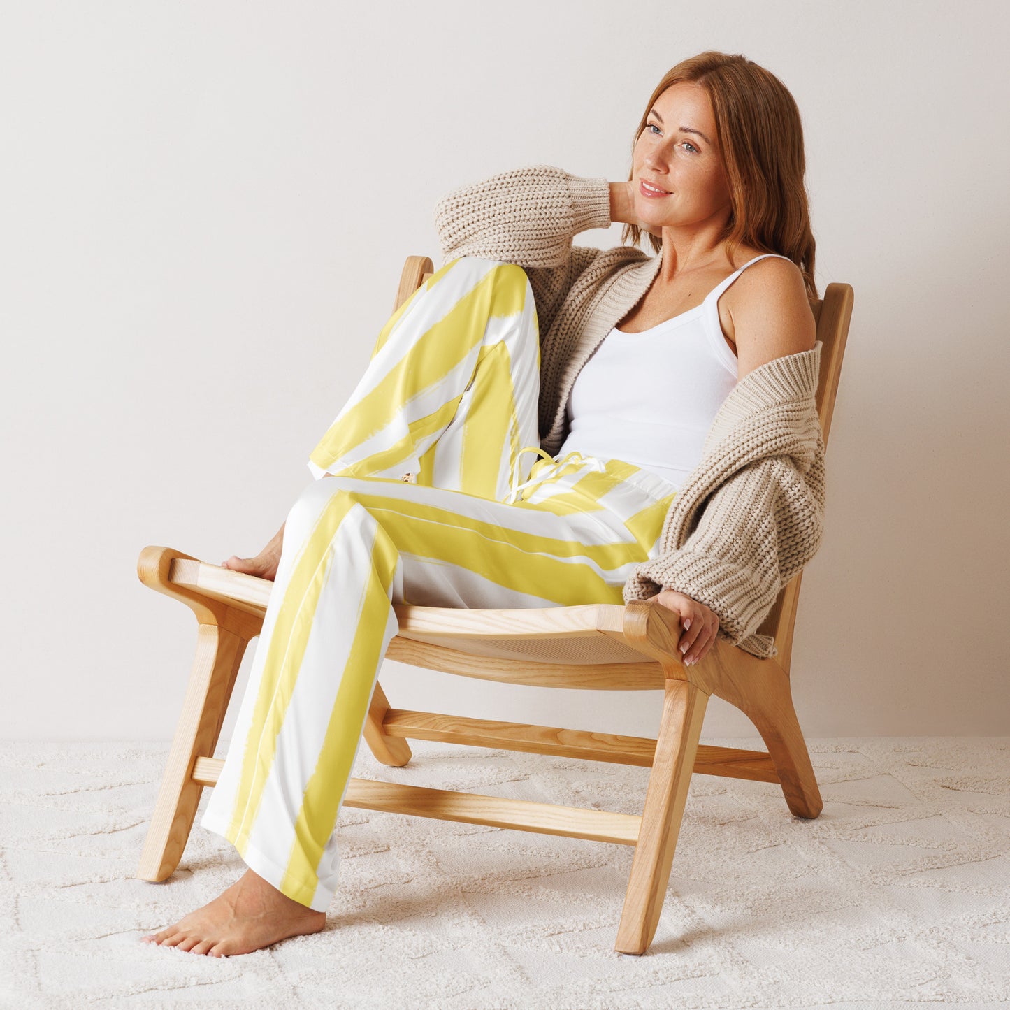 Woman lounging in chair wearing butter yellow striped pajama pants, styled with cardigan for cozy at-home wear or gifting.