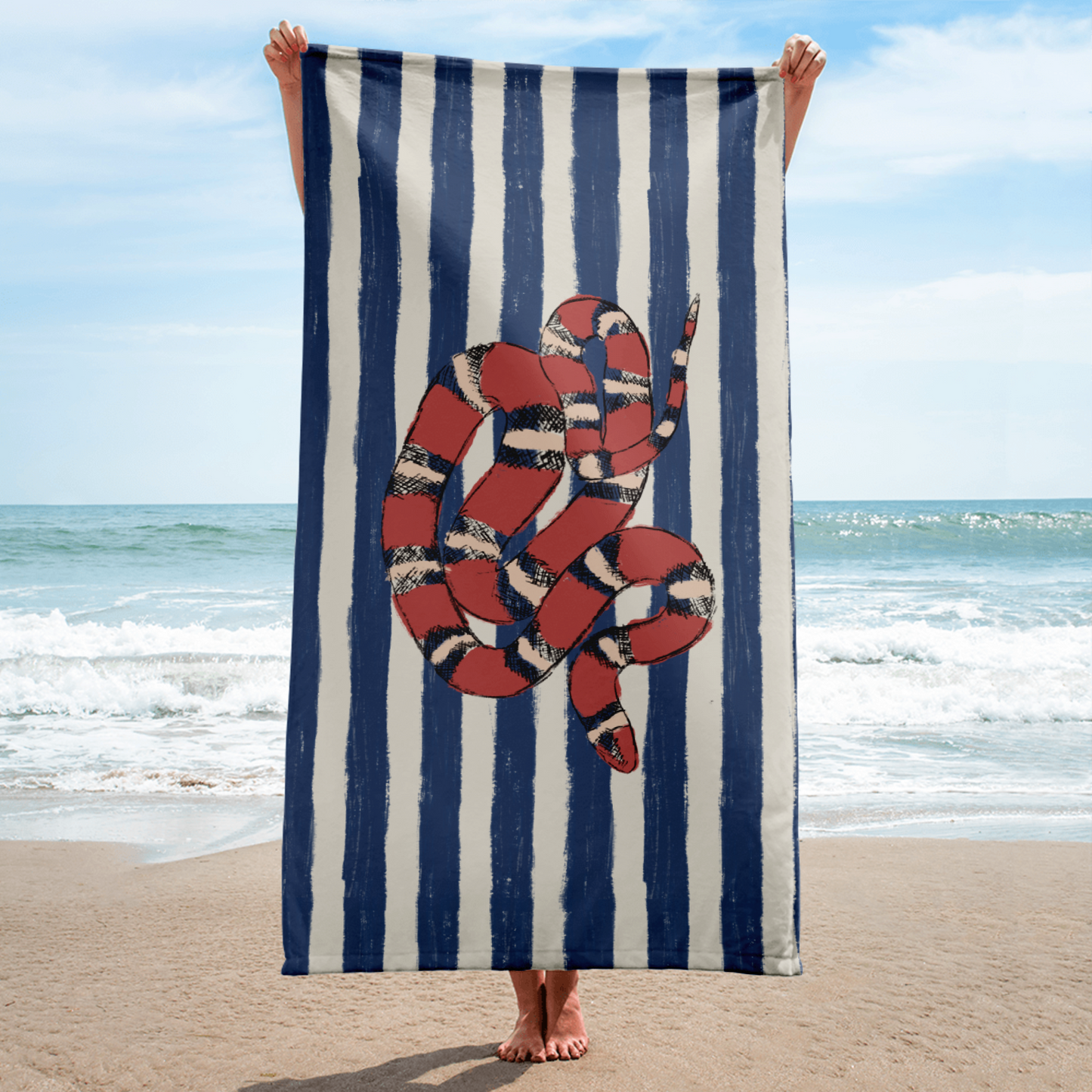 Vertical beach towel featuring red California kingsnake on blue and white stripes, held in front of ocean – snake print towel for coastal vacations