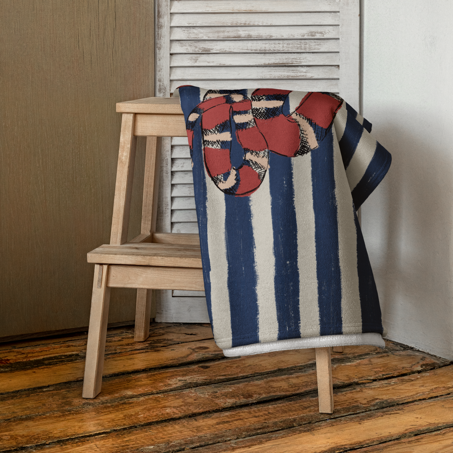 Snake print towel draped over wooden chair indoors, showcasing navy stripes and red snake design – luxury beach towel with bold graphic print