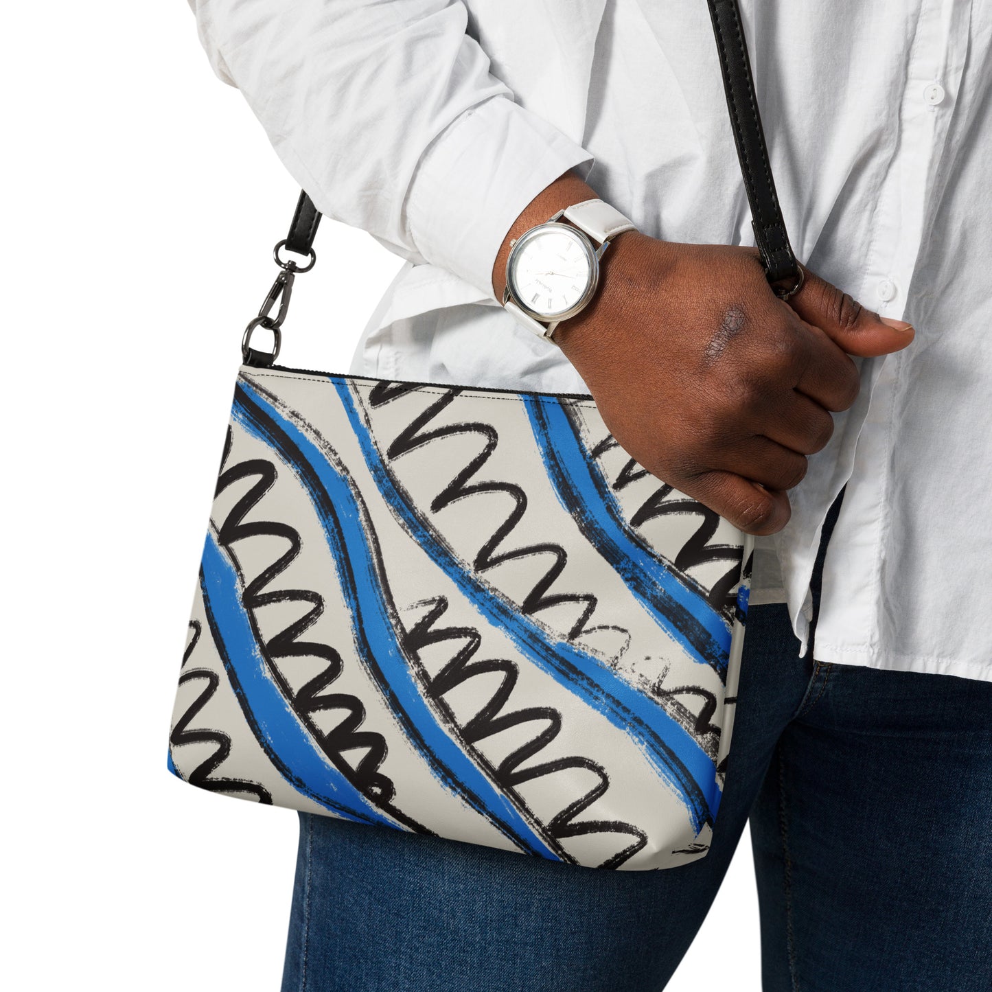 Crossbody bag worn on shoulder with abstract wave print in blue and black, styled with white shirt and blue jeans.