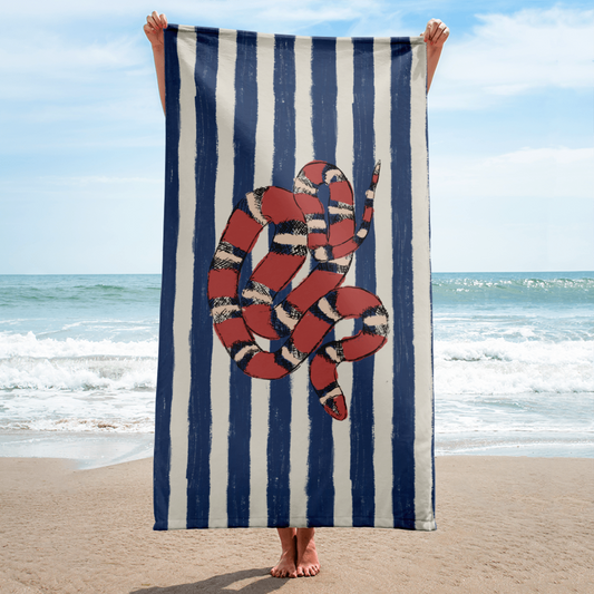 Vertical beach towel featuring red California kingsnake on blue and white stripes, held in front of ocean – snake print towel for coastal vacations